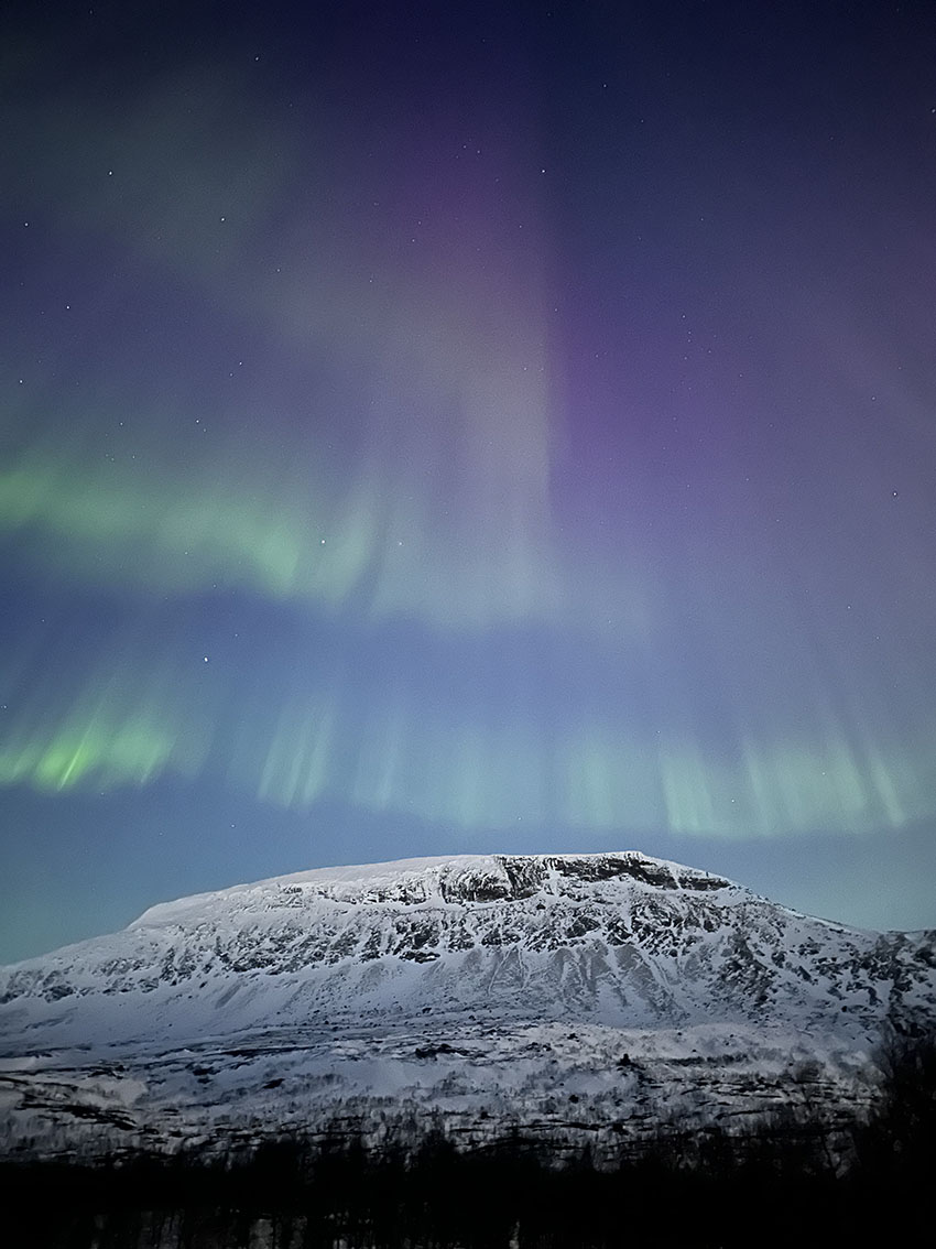 Nordlys i mange farger over en fjelltopp.